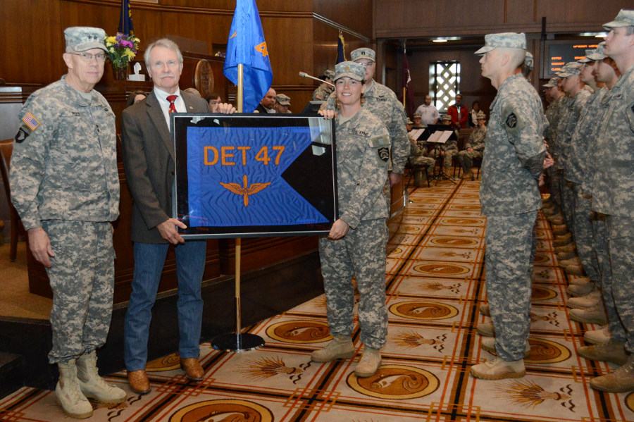 Oregon Governor John Kitzhaber accepts a framed unit guidon flag from Maj. Sarah Fritts (right), commander of Detachment 47, 2-641 Aviation, as Maj. Gen. Raymond F. Rees (left), Adjutant General, Oregon, looks on during the mobilization ceremony for two aviation units in the Senate Chamber at the State Capitol in Salem, Ore., Feb. 21. The governor keeps framed guidon's of deployed Oregon Army National Guard units until they return home to Oregon. Five Soldiers with Detachment 47, 2-641 Aviation, will deploy to Afghanistan in support of the Communications Electronic Attack with Surveillance and Reconnaissance (CEASAR) mission. (Photo by Staff Sgt. April Davis, Oregon Military Department Public Affairs)
